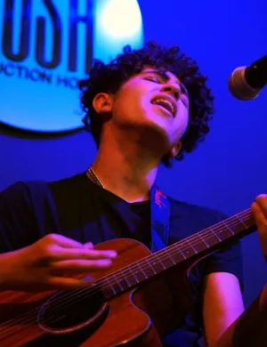Issam Al Najjar singing with his guitar under the Rush sign: Rush Local Music #1
